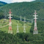 High voltage transmission towers stretching through lush green forest hills, showcasing energy infrastructure.