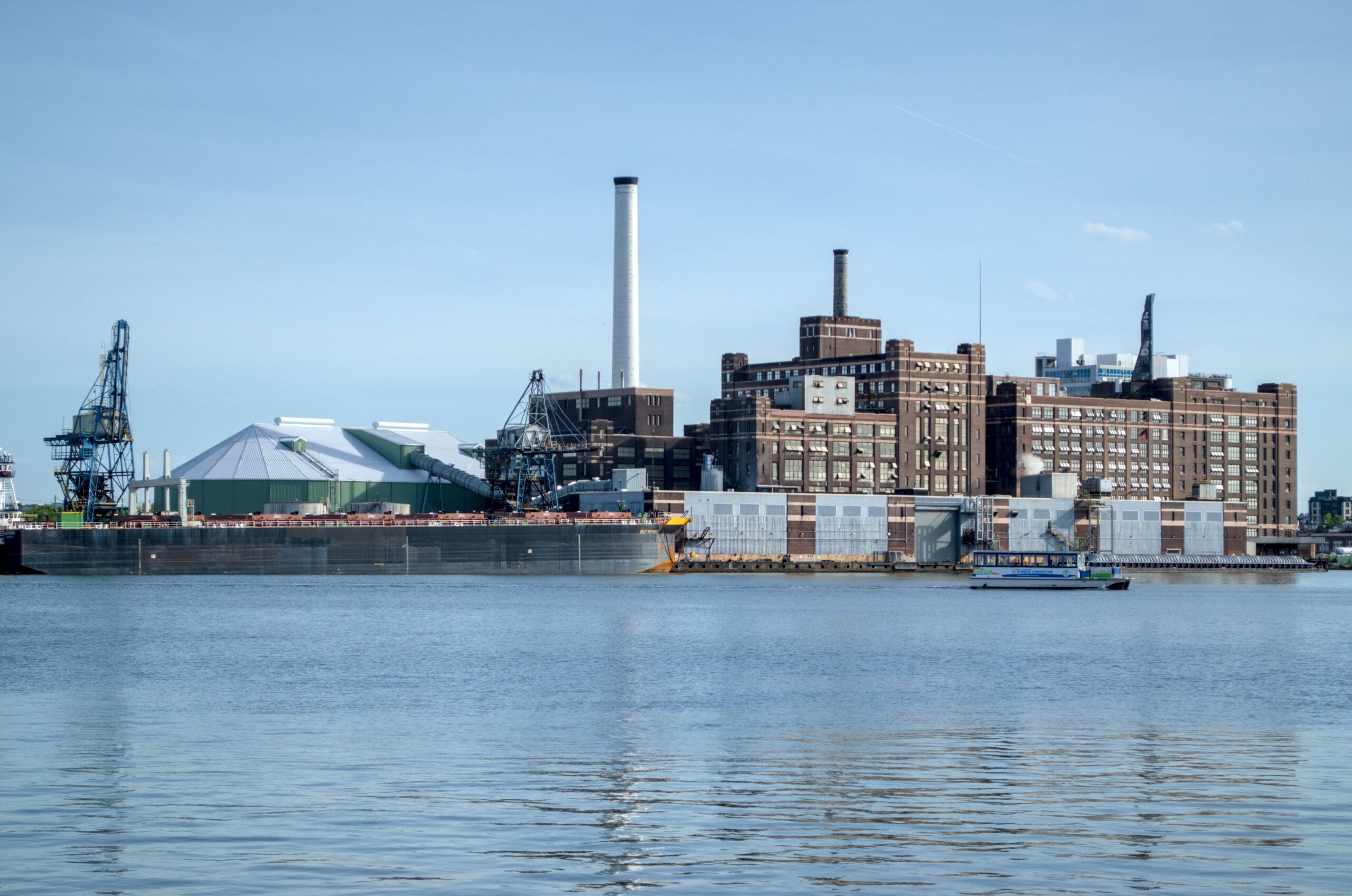 Aerial view of an industrial factory along Baltimore's waterfront under a clear blue sky.