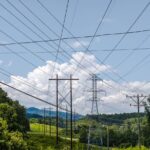 Overhead power lines crossing a lush green landscape under a bright summer sky.