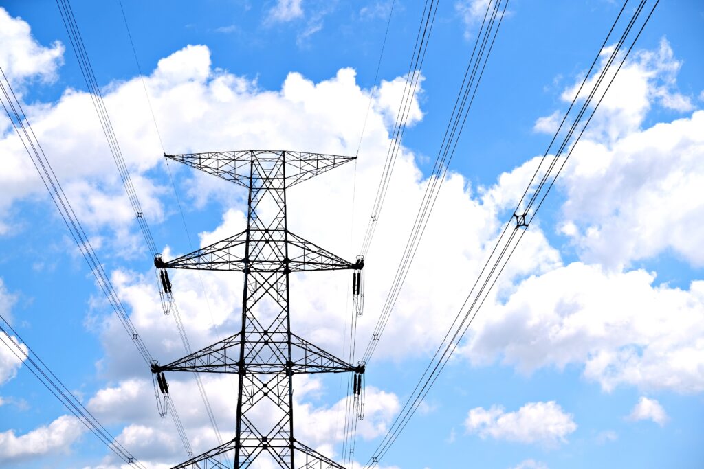 A view of high voltage power lines against a bright blue sky with fluffy clouds.
