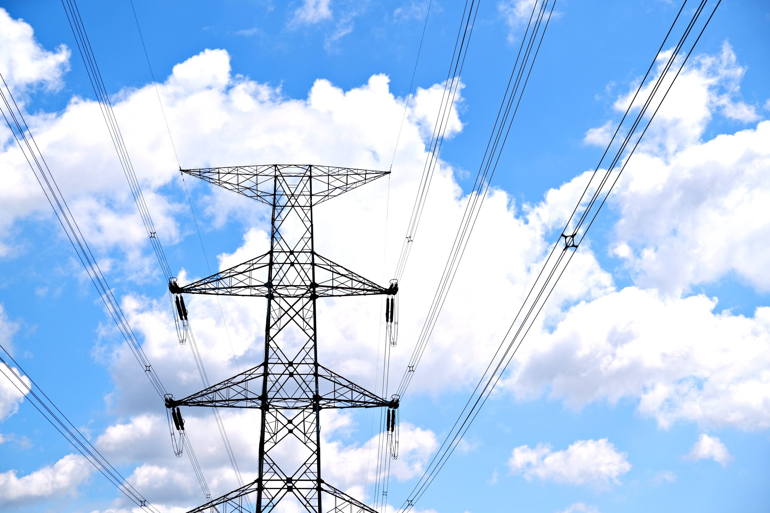 A view of high voltage power lines against a bright blue sky with fluffy clouds.